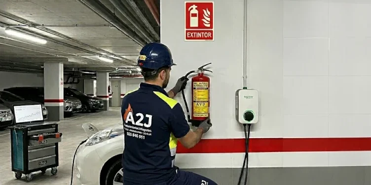 Técnico de A2J instalando un extintor especializado de Vermiculita (AVD) para fuegos de litio cerca de un cargador de coche eléctrico en Alcalá.