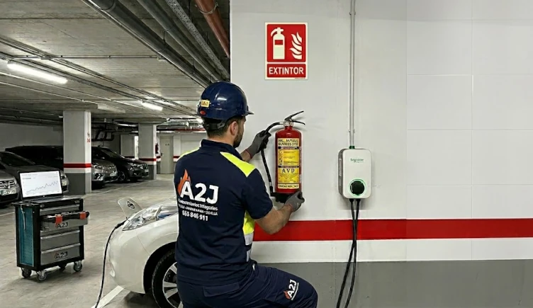 Especialistas en Protección Contra Incendios para Cargadores de Coche Eléctrico en Alcalá. Técnico de A2J instalando un extintor especializado de Vermiculita (AVD) para fuegos de litio cerca de un cargador de coche eléctrico en Alcalá.